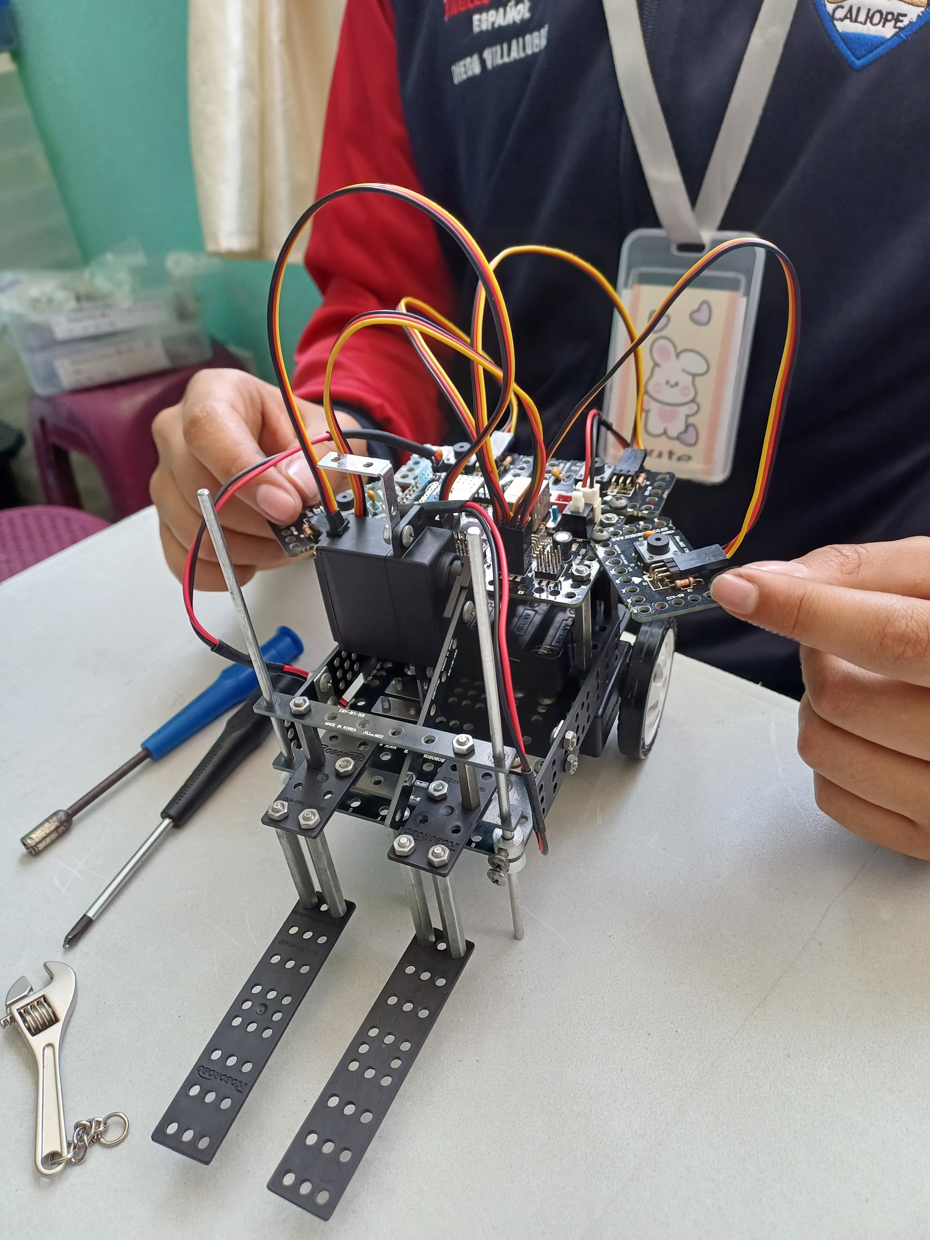Estudiante ensamblando un robot con motores, cables y estructura metálica en un taller de robótica de ItEduca Friends